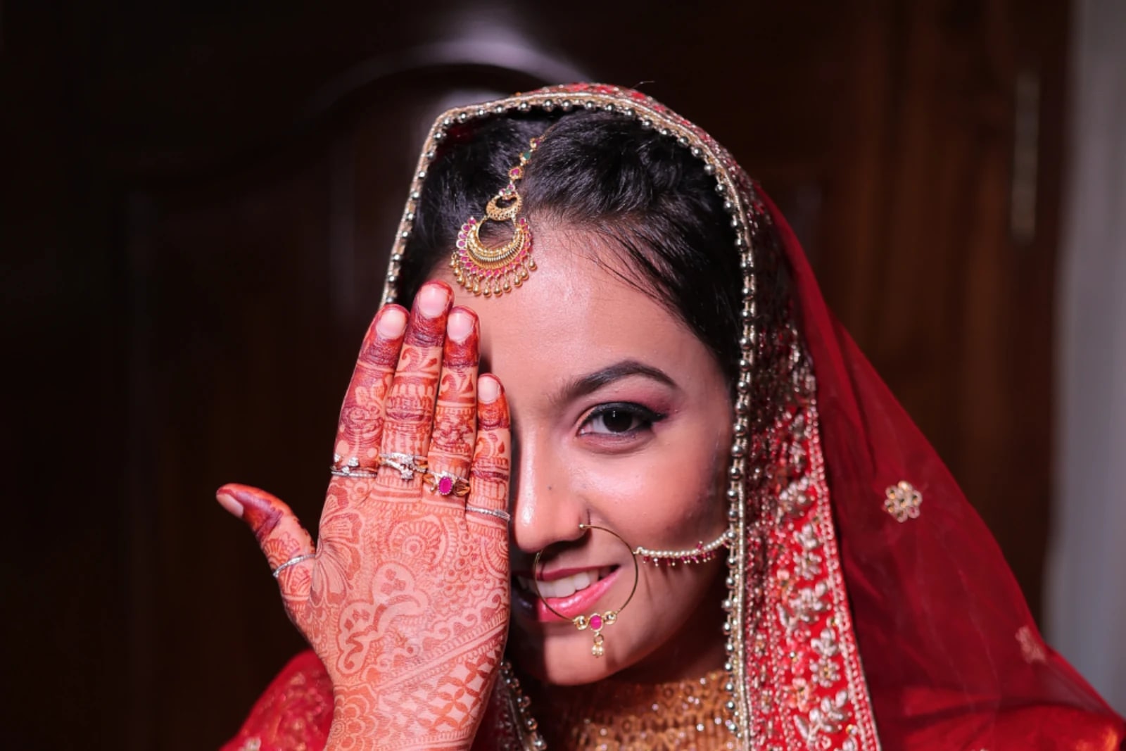 Bride in red covering one eye with her decorated hand